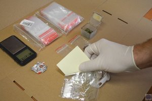 Policjant waży narkotyki, na stole puste woreczki strunowe oraz pudełko z zielonym suszem w środku