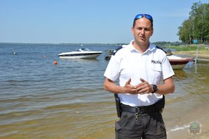 policjant ogniwa wodnego stoi na plaży w tle jezioro i łódka