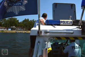 policyjna łódź motorowa dopływa do pomostu, jeden policjant stoi na burcie drugi siedzi za sterami