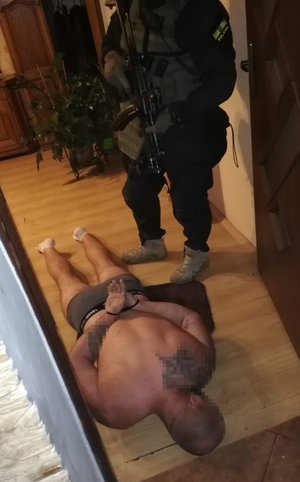 zatrzymany mężczyzna leży z założonymi kajdankami, a nad nim stoi policyjny kontrterrorysta