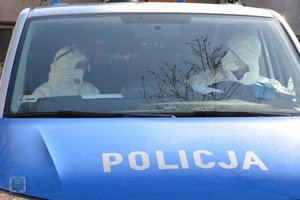 policjanci ubrani w kompletny strój  ochronny siedzą w radiowozie