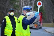 policjant z kamizelką odblaskową i maseczką na twarzy pokazuje w wyciągniętej ręce czerwony sygnalizator do zatrzymywania pojazdów